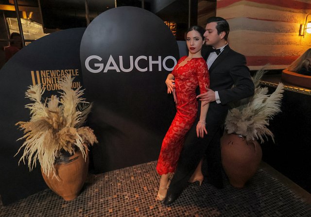Woman in red dress and man in tuxedo posing, preparing to tango dance