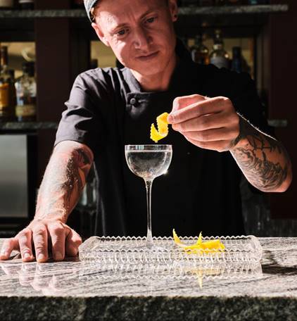 Man garnishing a cocktail with a twist of lemon peel