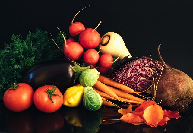 An assortment of vegetables against a black background, tomatoes, cabbage, Brussells sprouts, aubergine, beetroot, radishes, 'irresistible vegetables' food trend